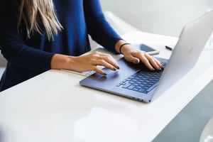 Frau tippt auf einem Laptop am weißen Schreibtisch